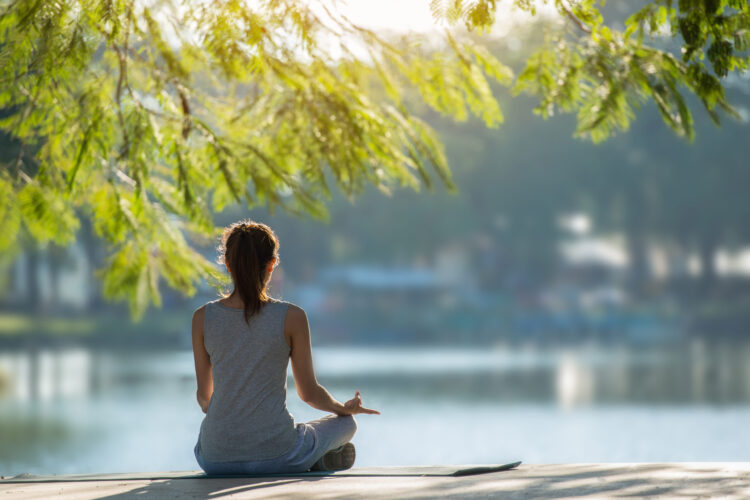 Beautiful woman practicing yoga waterfront in the park.