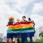 Lgbtqia+ friends embracing and holding a rainbow flag outdoors