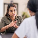 Woman sitting at a table speaking seriously with a healthcare professional, discussing something important during a counseling or medical session.
