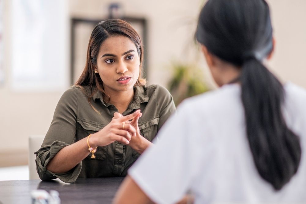 Woman sitting at a table speaking seriously with a healthcare professional, discussing something important during a counseling or medical session.