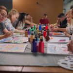 Group of adults sitting around a table engaged in art therapy, painting colorful designs on paper as a form of creative expression.