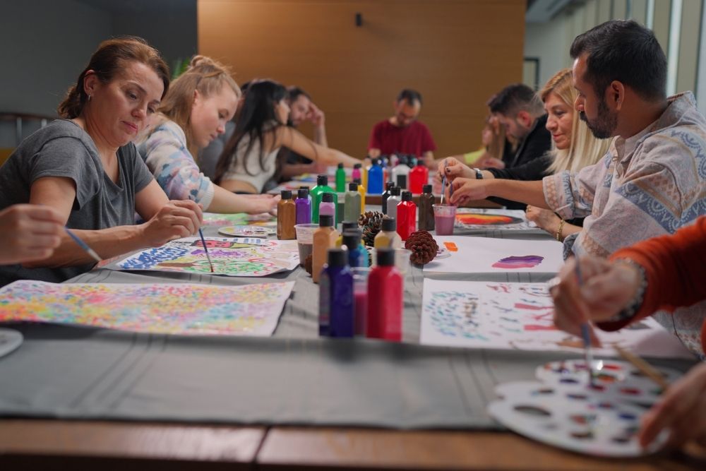 Group of adults sitting around a table engaged in art therapy, painting colorful designs on paper as a form of creative expression.