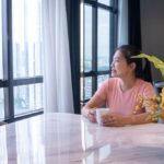 2. A woman at a table, enjoying a coffee cup, with a calm demeanor and a cozy atmosphere around her.