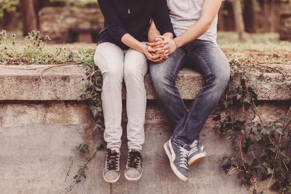 Carolina Dunes - Teen Dating Violence Prevention Month - Edited. Two youth sit outdoors holding hands with one another.